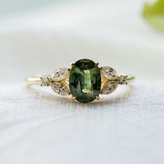 an oval green tourmaline surrounded by three pear shaped diamonds on a white cloth