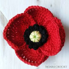 a crocheted red flower sitting on top of a white table next to a button