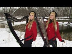 two beautiful young women standing next to each other in the snow holding harps and looking at camera