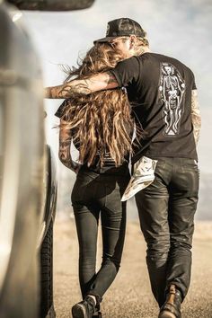 a man and woman standing next to each other in front of a car with long hair