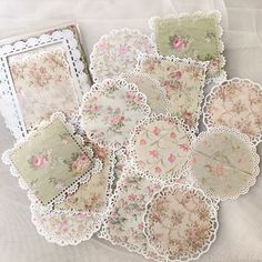 several pieces of paper with lace and flowers on them sitting on a white table cloth