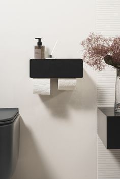 a black toilet sitting next to a white wall with a vase filled with flowers on it