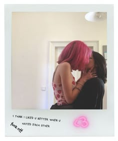 a woman with pink hair is kissing another woman's face in front of a mirror