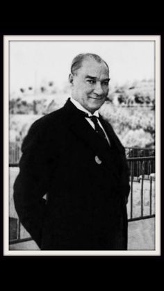 an old photo of a man in a suit and tie standing next to a fence