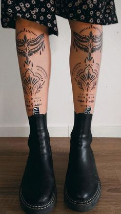 the legs and ankles of a woman with tattoos on her leg, wearing black rubber boots