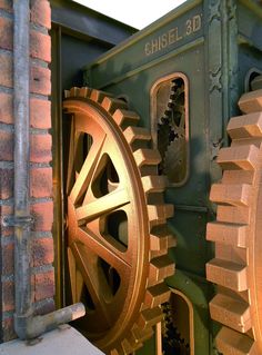 a close up of a large metal object with gears on it's side and another piece of machinery in the background