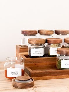 several jars with labels on them are sitting on a wooden tray next to a candle