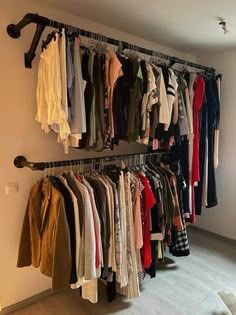 an organized closet with clothes hanging on the wall and coat racks in front of it