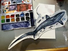 a watercolor painting of a shark on a piece of paper next to paintbrushes