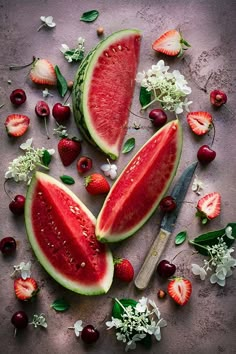 watermelon slices and strawberries on a table with flowers, leaves and berries