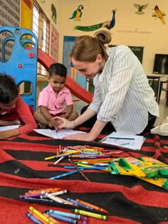 a woman and two children sitting at a table with crayons on the floor