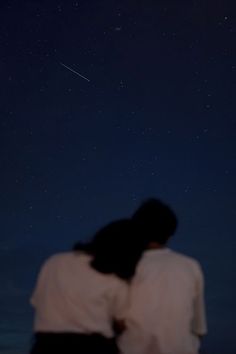 two people are looking up at the stars in the night sky, with one person holding his arm around the other