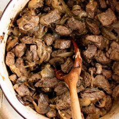 a pot filled with meat and onions next to a wooden spoon on top of a table