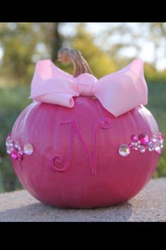 a pink pumpkin with a monogrammed bow on it's head sitting on a rock