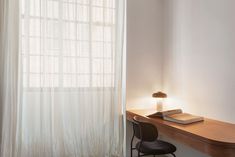 a desk with a book and lamp on it in front of a curtained window