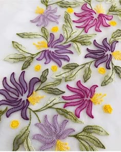 some very pretty purple and yellow flowers on a white table cloth with green leaves in the middle