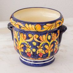 a blue and yellow flower pot sitting on top of a white table next to a wall