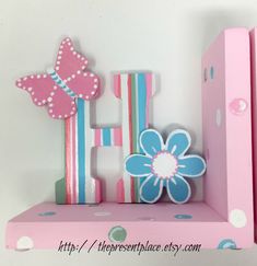 a pink and blue wooden letter with flowers on it's sides sitting on a shelf