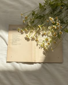 an open book sitting on top of a bed next to a bouquet of wildflowers