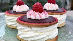 three desserts with raspberries and whipped cream on top are sitting on a plate