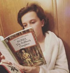 a woman reading a book in front of a wooden wall