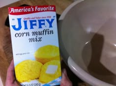 a person holding up a carton of corn muffins next to a bowl