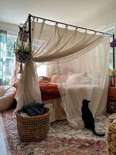 a cat sitting on the floor in front of a canopy bed with curtains over it