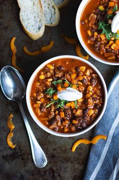 two bowls of chili with sour cream on top and bread in the backgroud