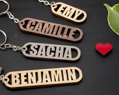 three wooden key chains with the names of two people and a red heart on them