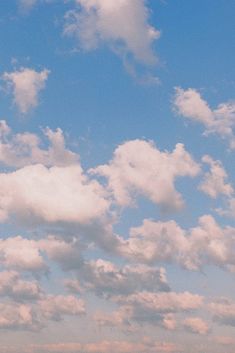 two people standing on the beach flying a kite in the blue sky with white clouds