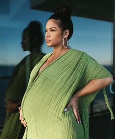 a woman in a green dress standing next to a window with her hands on her hips