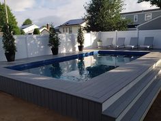 an empty swimming pool in the middle of a backyard with lounge chairs and potted trees