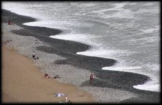 people are on the beach with an umbrella and waves crashing in to shore as seen from above