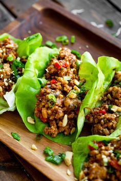 lettuce wraps filled with meat and vegetables on a cutting board next to a wooden tray