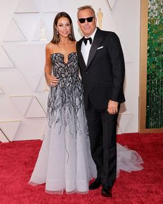 an older man and woman in formal wear posing on the red carpet