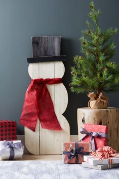 a snowman made out of wood sitting next to presents and a small christmas tree