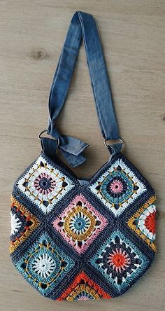 a crocheted purse hanging on a wooden floor with a blue ribbon around it