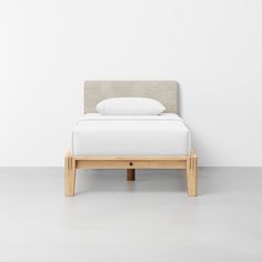 a bed with a wooden frame and white sheets on the headboard, sitting in front of a wall