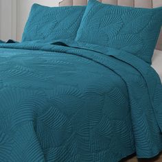 a bed covered in a teal blue quilt and pillow cases with matching pillows on top