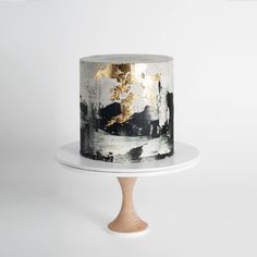 a black and white cake with gold leaf decorations on top, sitting on a wooden stand