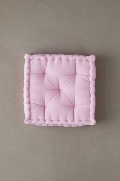 a pink square cushion with scalloped edges on a gray wall, viewed from above