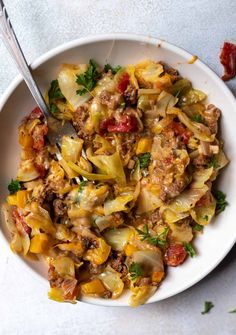 a white bowl filled with pasta and meat on top of a marble counter next to a fork