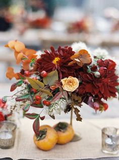 a vase filled with flowers and oranges on top of a table next to glasses