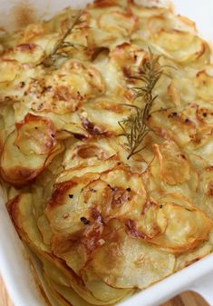 baked potato casserole with rosemary sprig in white dish on wooden table