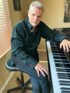 a man sitting at a piano with his hands on the keyboard and looking into the camera