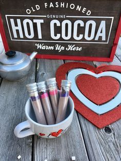 hot cocoa in a cup next to a sign and other items on a wooden table