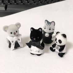 four small stuffed animals sitting next to each other on a white tablecloth with keyboard in the background