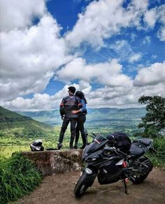 two people standing next to a motorcycle on top of a hill