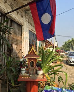 a flag hanging from the side of a building next to plants and potted plants