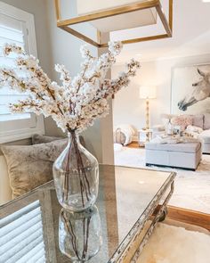 a glass vase with white flowers on a table in front of a living room window